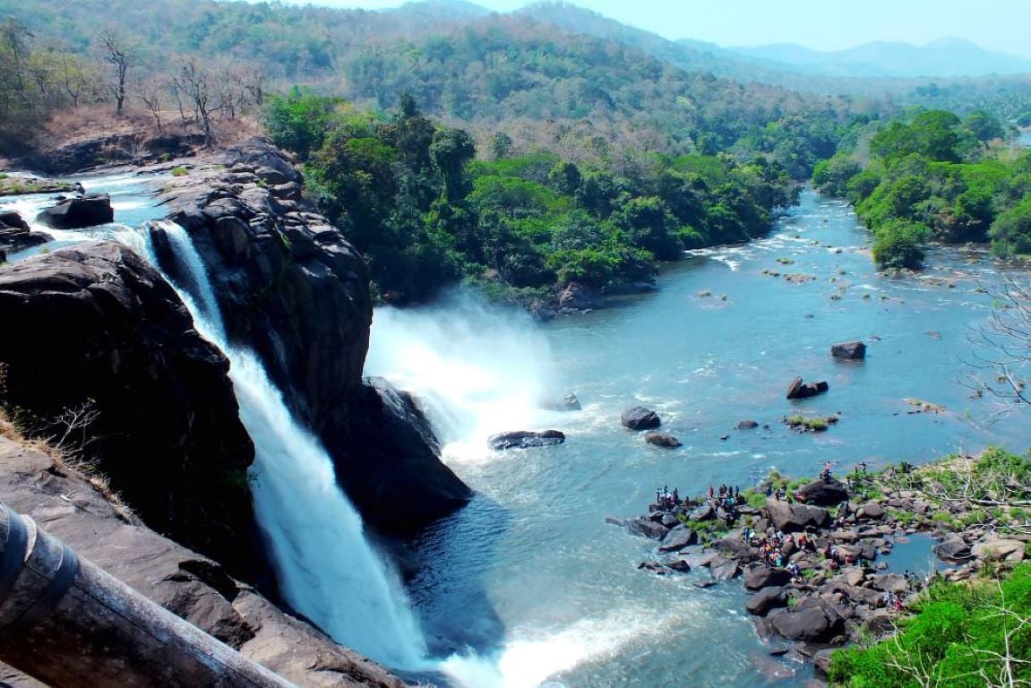 Athirappilly waterfall flowing into a forest-lined river in Kerala