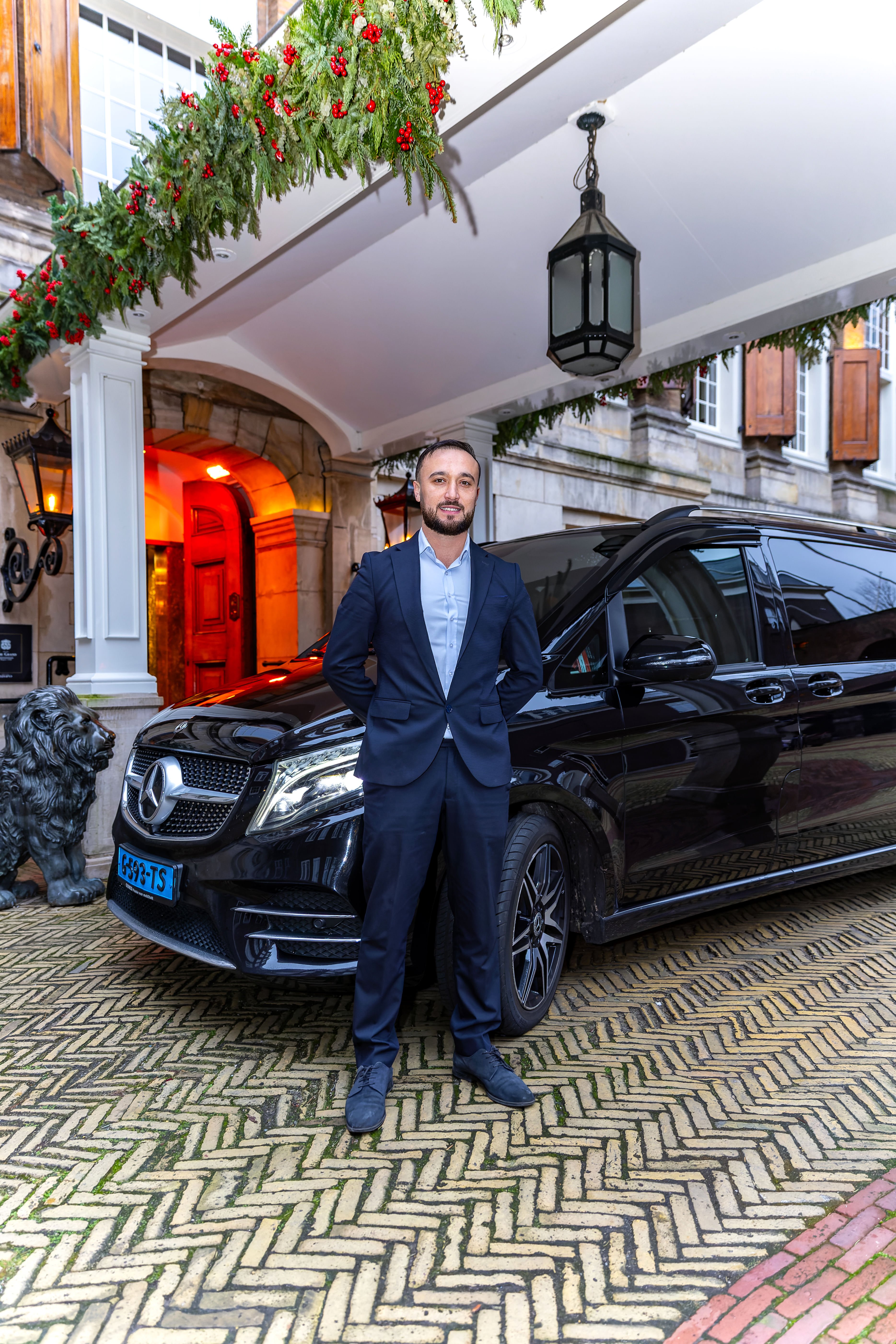 Taxi driver in front of his taxi and a renowned hotel