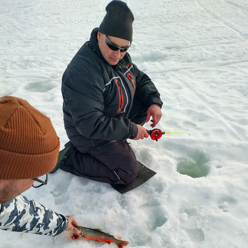 Two men doing ice fishing and measuring the catch