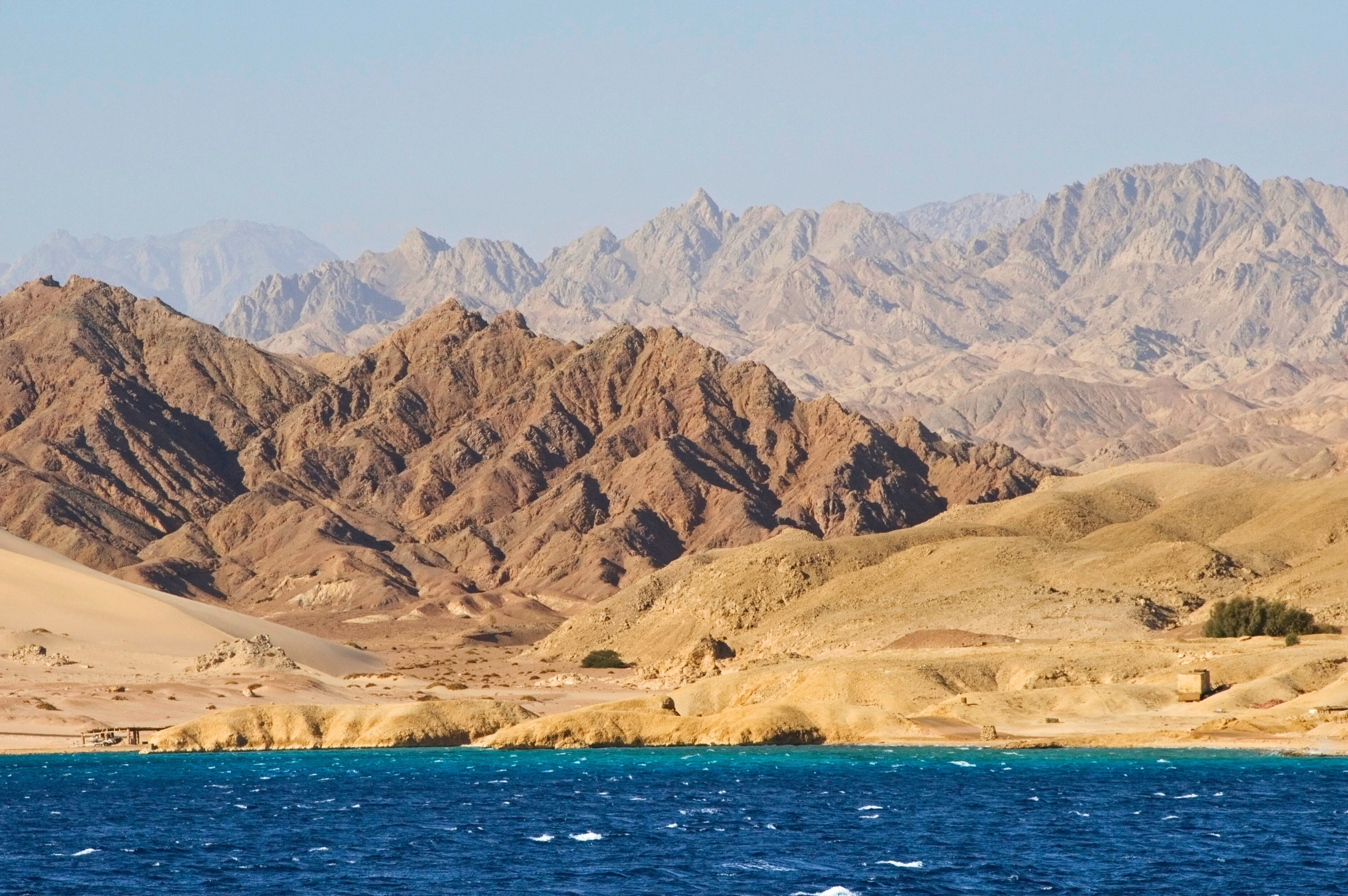 Majestic, layered Sinai desert mountains meeting the vibrant, deep blue waters of the Red Sea coastline near Ras Muhammad national park
