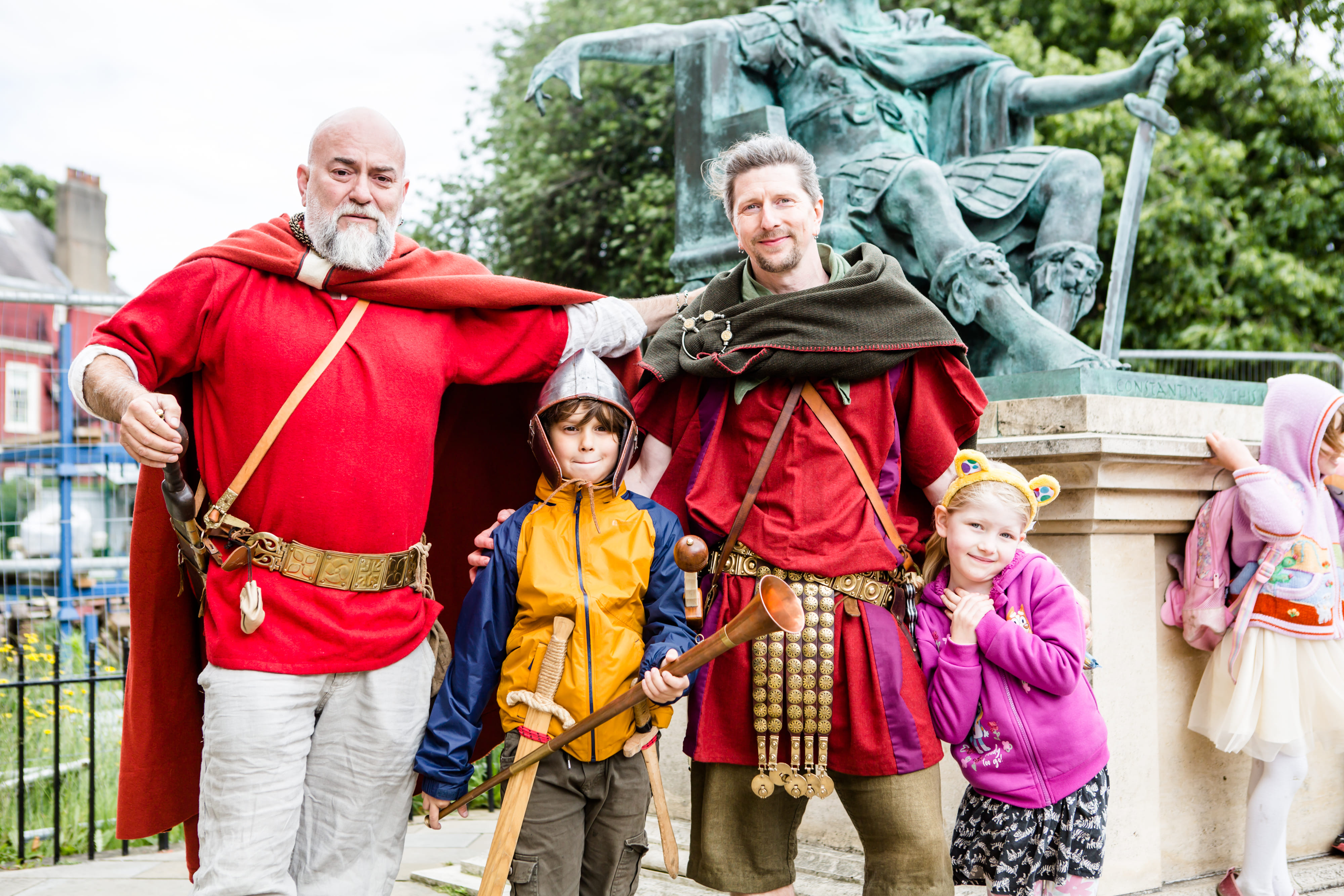Two mighty Romans tower over a young boy and girl. The boy is armed with a sword, helmet, and Roman tuba. The girl has Pudsey Bear ears on.