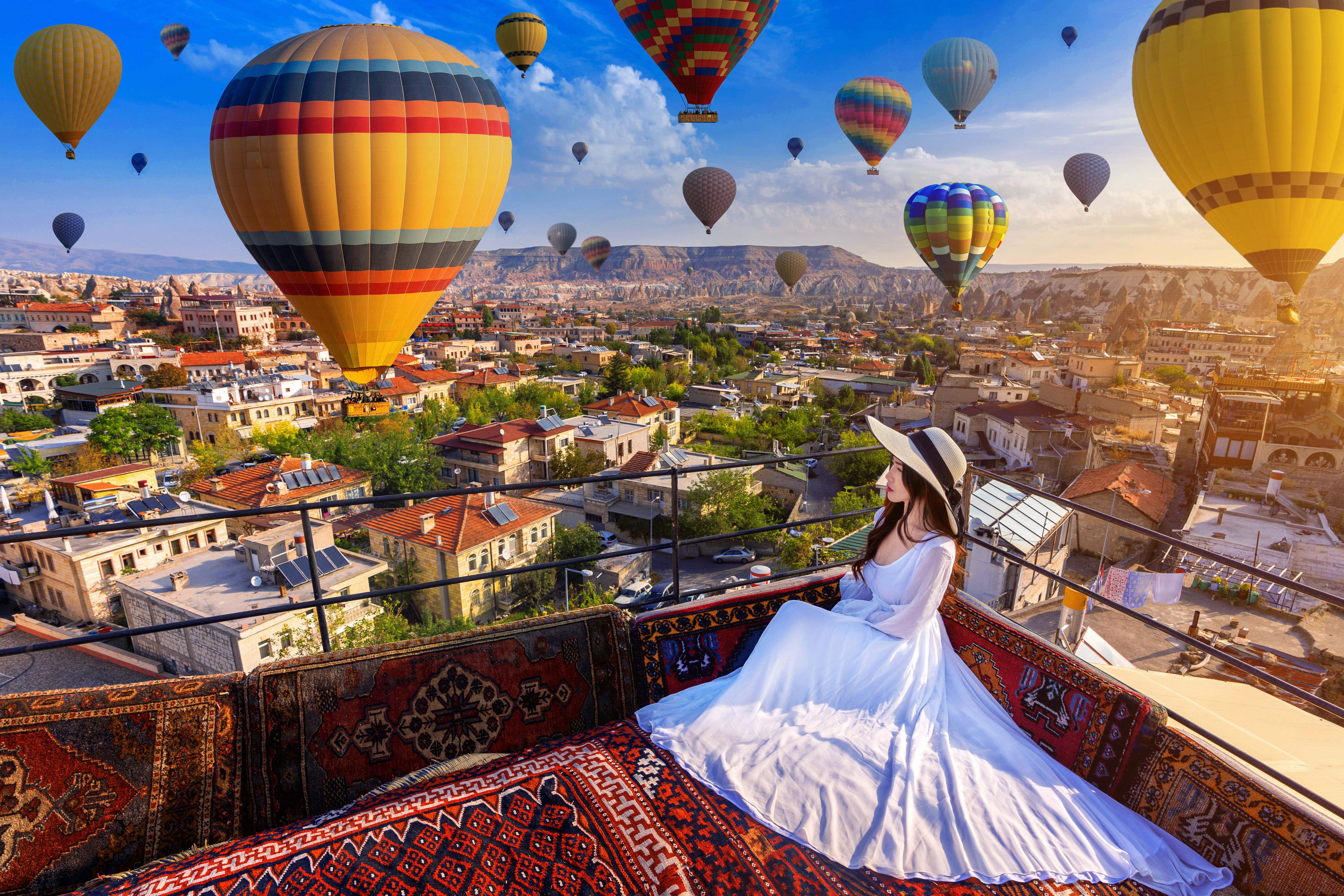 “Spectacular view of colorful hot air balloons drifting over the unique rock formations of Cappadocia, seen from a hotel terrace at sunrise.