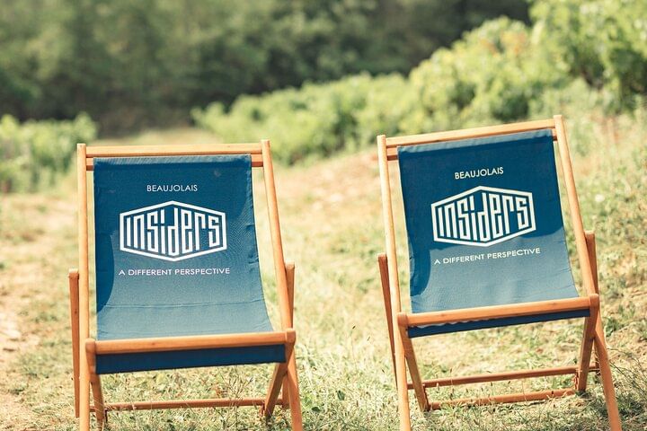 Two beach lounge chairs, the fabric printed with the Beaujolais Insiders logo, are set in the middle of a vineyard on a bright summer's day