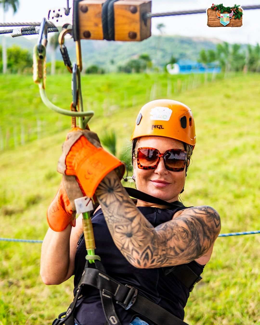 Woman wearing a helmet, gloves, and safety gear gliding on a zip line in Punta Cana, smiling as she enjoys the adventure, surrounded by lush