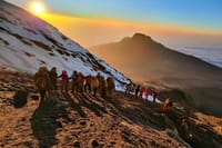A group of hikers walking along a snowy mountain ridge during a golden sunrise.