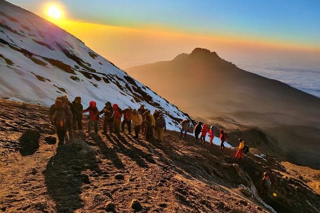 A group of hikers walking along a snowy mountain ridge during a golden sunrise.