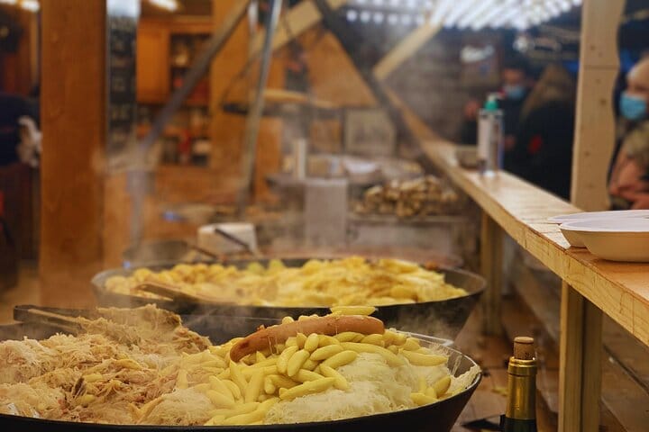 Traditional Alsatian dishes (sauerkraut, sausage, Spätzle) steaming in large pans at the Place Broglie Christmas Market.