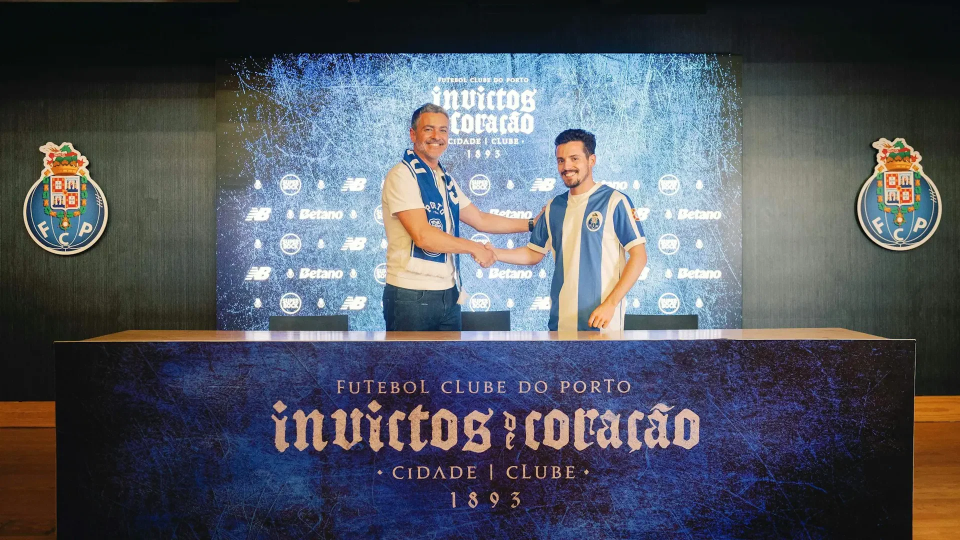 Two men shake hands over a wooden desk in front of a branded backdrop featuring text and crests at FC Porto Museum & Dragão Stadium ticket.