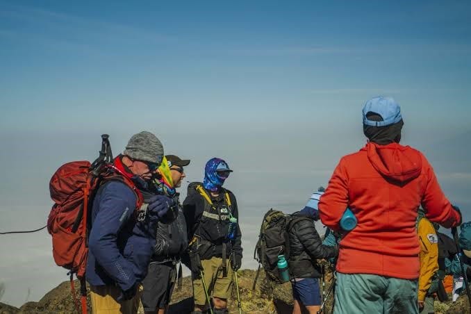 A group of hikers with backpacks gathered together on a high mountain trail under a clear sky.