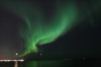Bright green Northern Lights appearing over the ocean during a peaceful evening boat tour from Reykjavík, Iceland.