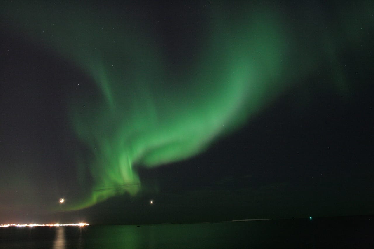 Bright green Northern Lights appearing over the ocean during a peaceful evening boat tour from Reykjavík, Iceland.