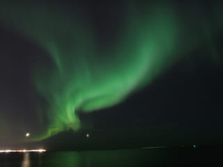 Bright green Northern Lights appearing over the ocean during a peaceful evening boat tour from Reykjavík, Iceland.