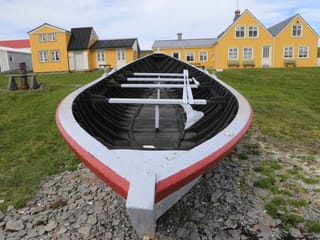 Bright yellow wooden farmhouses behind a large wooden open boat in the foreground