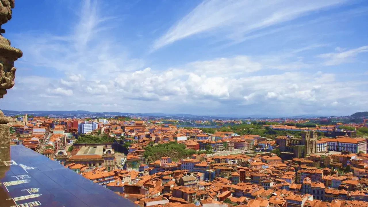 A high-angle vista reveals a vast expanse of city buildings with terracotta roofs under a dramatic sky with wispy clouds at Clérigos Tower & Museum Ticket.
