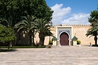 Monumental gate and historical ramparts of Fez, surrounded by gardens and palm trees, illustrating traditional Moroccan architecture and the prestige of the imperial city.
