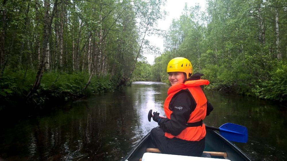 A person canoeing on river Pyhäjoki with green forest on sides