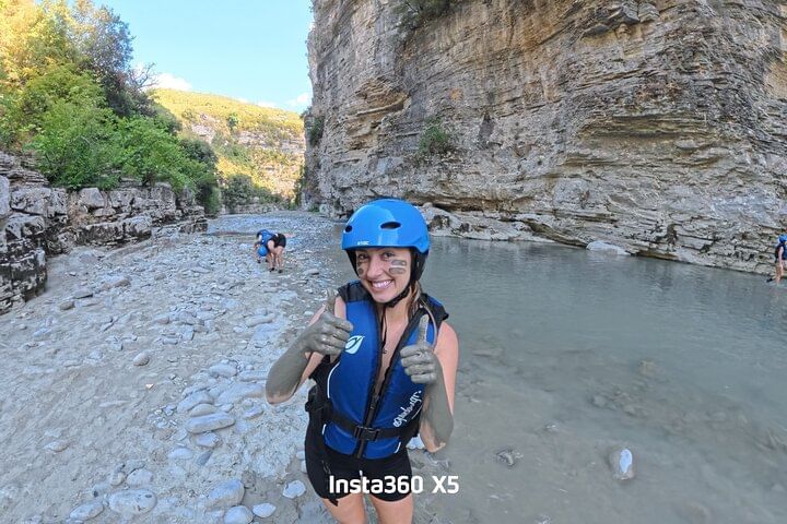 A person in a helmet and life vest smiling while standing in a rocky canyon river .