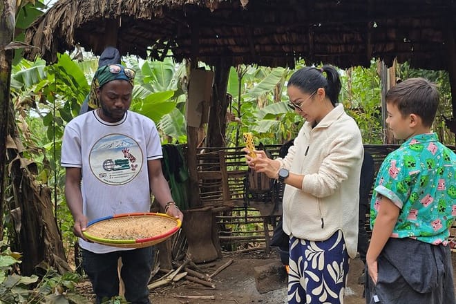A local guide and a tourist using a traditional woven tray to winnow coffee beans in a sunlit garden.