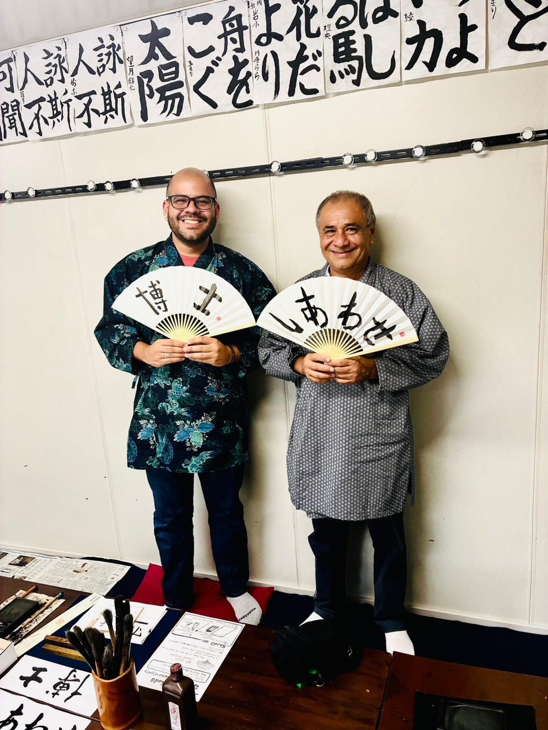 Two foreign tourists wearing traditional Japanese coats and holding custom calligraphy folding fans