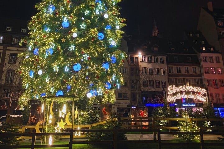 Illuminated Great Christmas Tree (stars, moons, ornaments) at night in Place Kléber. It is surrounded by small wooden fences.