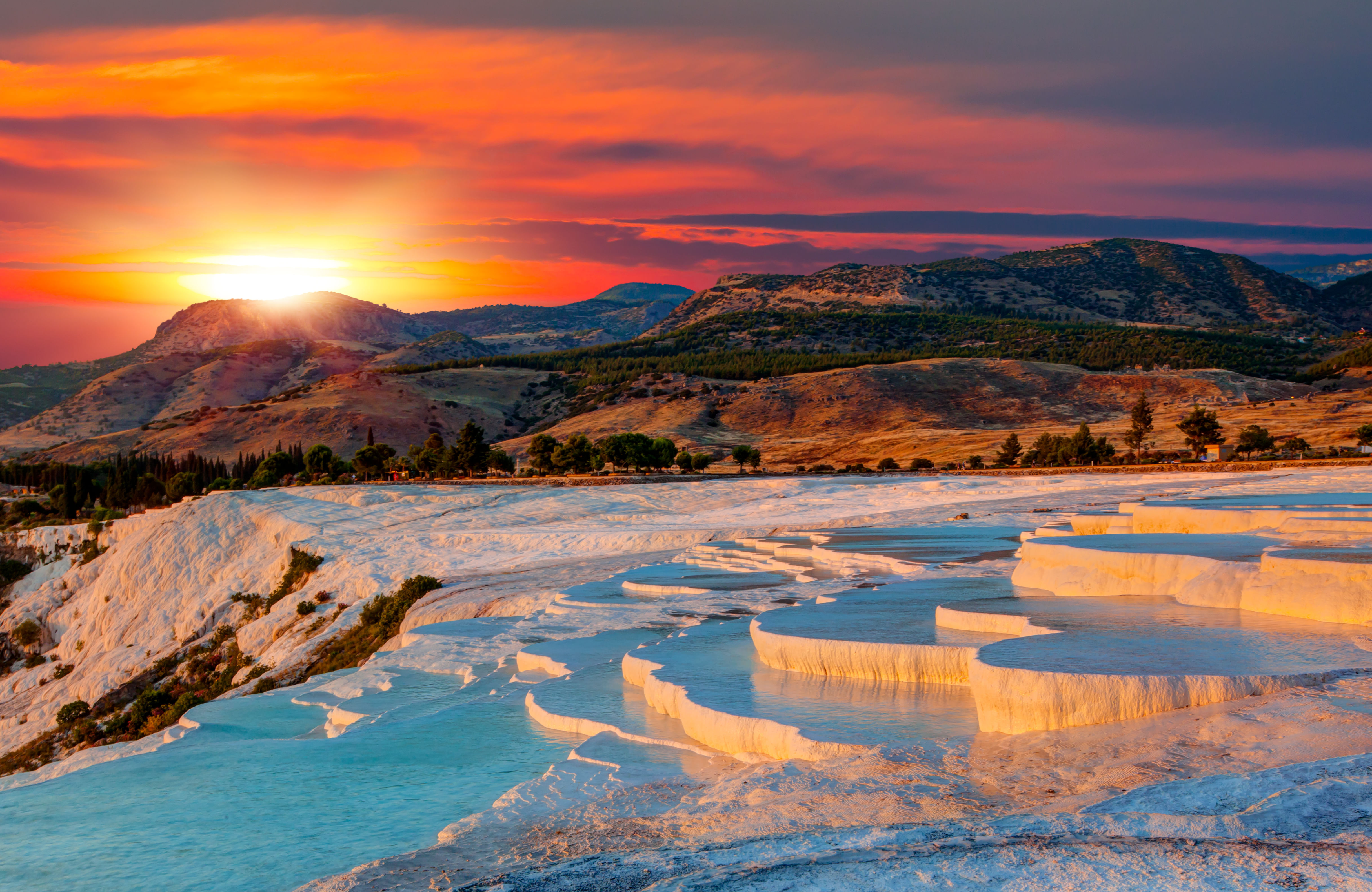 “Pamukkale’s white travertine terraces filled with turquoise thermal water, glowing under the golden and pink light of sunset.”