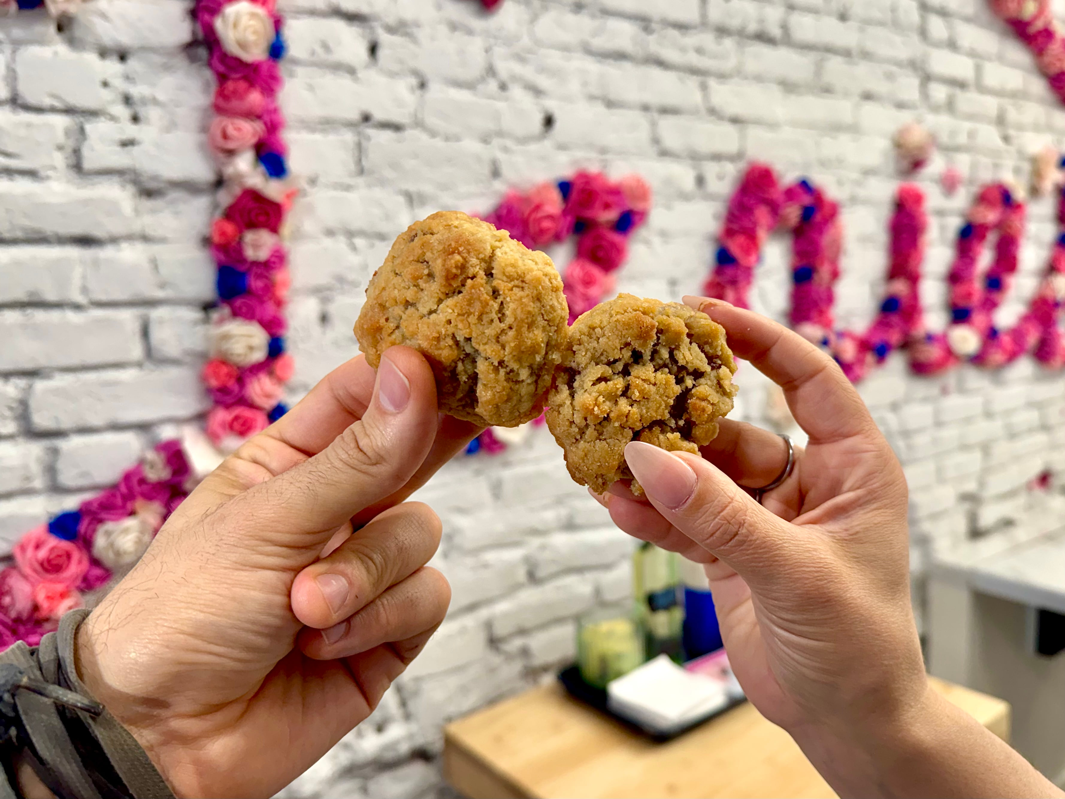 Two people hold up partially eaten pie crust cookies in front of a floral sign.