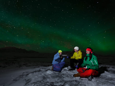 Three people enjoying the skies during Arctic adventures northern lights tour
