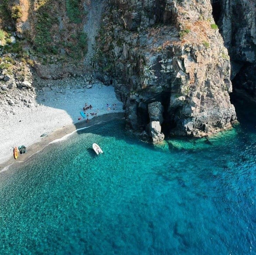 Aerial view of a boat sailing on the clear blue waters along the Costa Viola