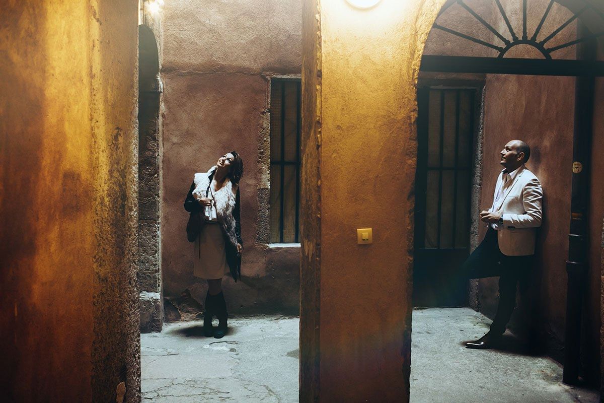 Two people exploring a dimly lit traboule in Lyon, surrounded by warm-toned historic walls and archways, evoking a sense of mystery and hist