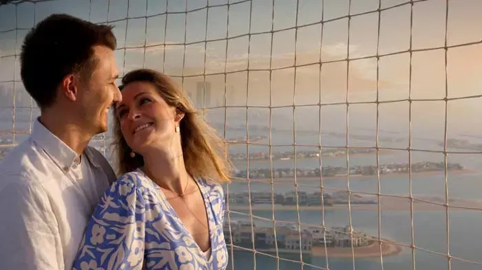 A smiling couple stands inside a netted observation enclosure overlooking water and distant land at The Dubai Balloon at Atlantis.