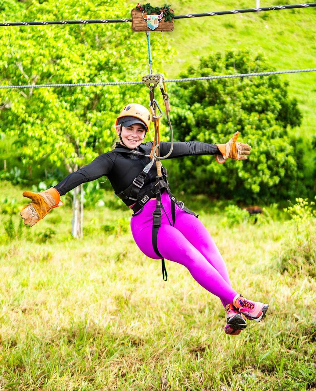 Smiling woman wearing a helmet and safety gear enjoying a zip line experience in Punta Cana, gliding above lush tropical greenery.