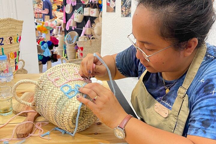 Participant carefully embroidering colorful letters on a palm-leaf basket during the workshop in Marrakech.