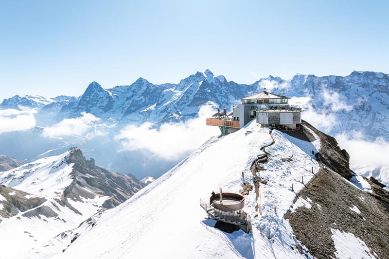 O Piz Gloria acima de um mar de nuvens, com os Alpes no horizonte.