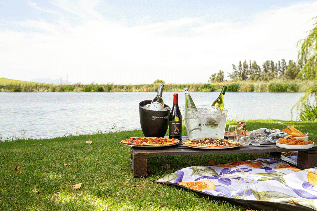Gourmet picnic basket and bottle of Flatrock wine on a low wooden table on the lawns of Rhebokskloof Wine Estate, Paarl.