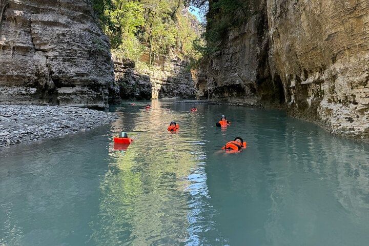 Group of people enjoying the turquoise river in Osumi Canyon with tall rock walls on each side.