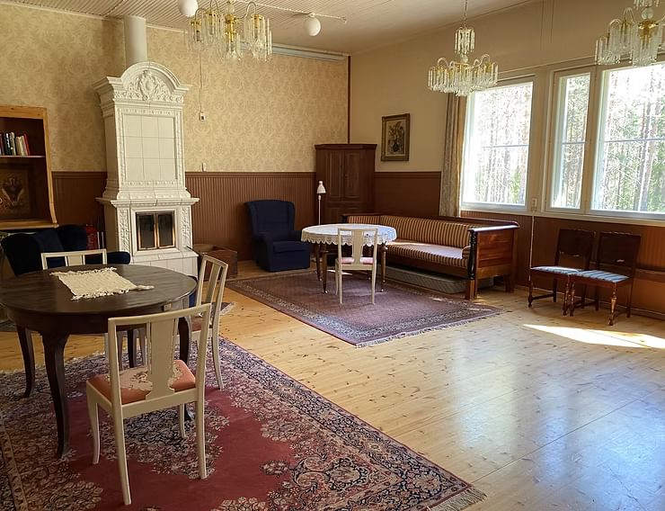 Spacious, sunlit guesthouse lounge with wooden floors, antique furniture, chandeliers, and a traditional white fireplace