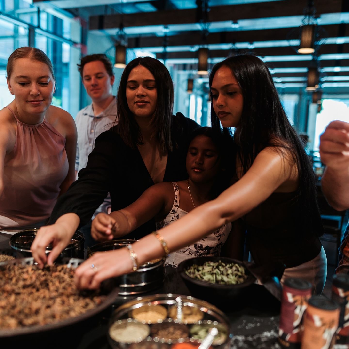 A group of five smiling participants enthusiastically gather and select spices and ingredients during a hands-on Cape Malay cooking class.