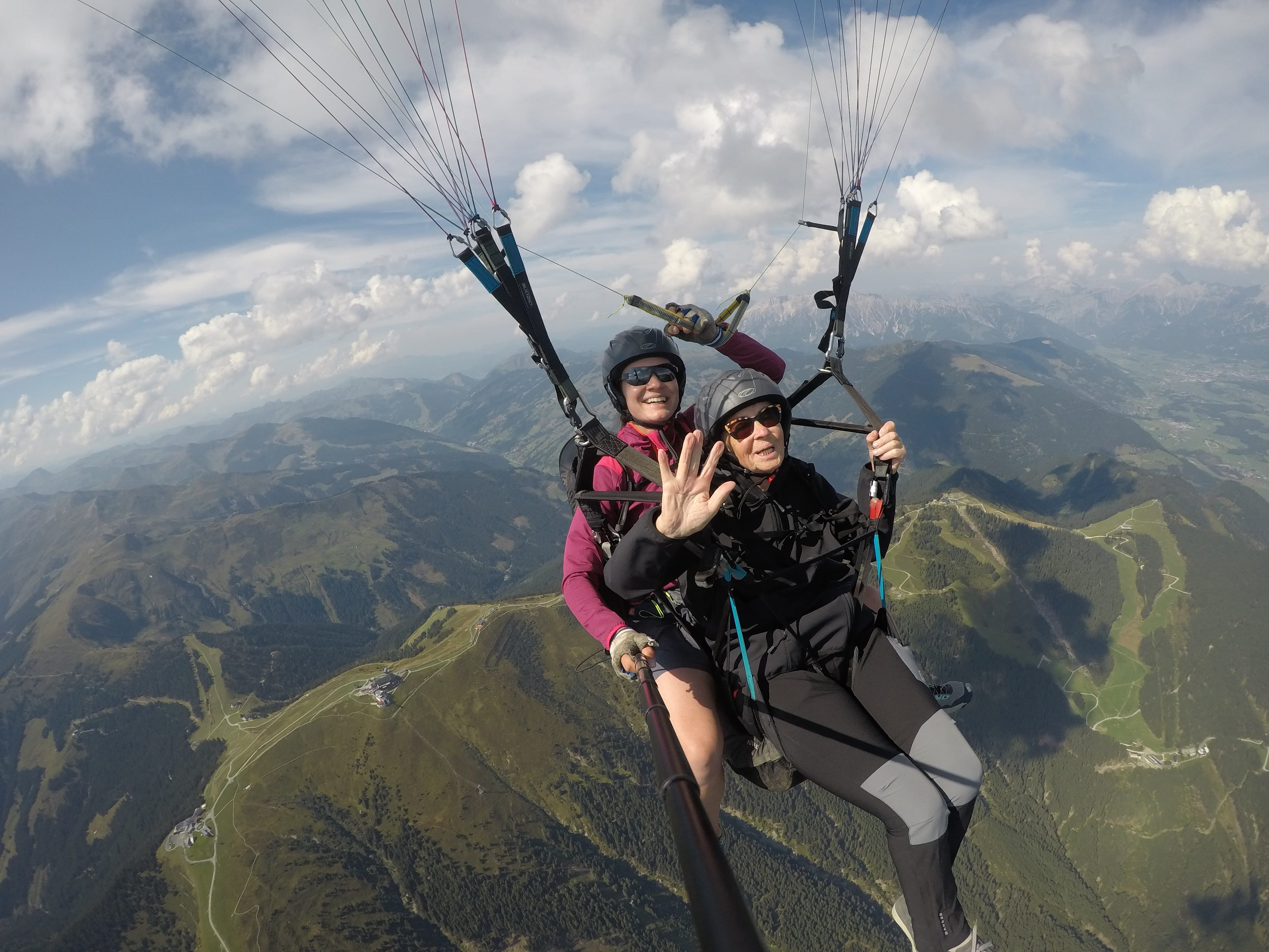 An elderly woman paragliding with a female tandem pilot high above Schmittenhöhe, Austria