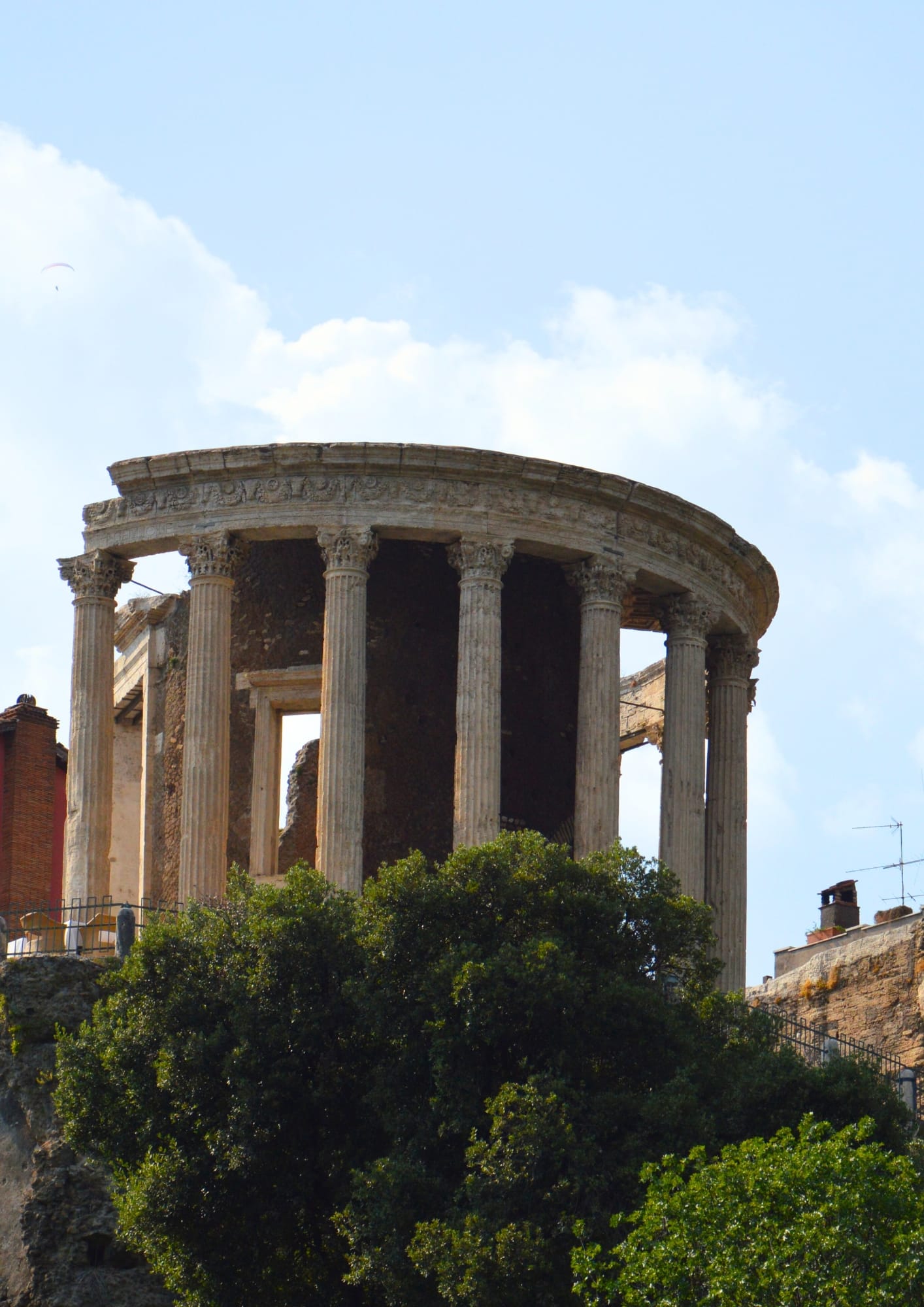 The Temple of Vesta in Tivoli, a circular Roman shrine with columns, set above ancient stone walls and pines.