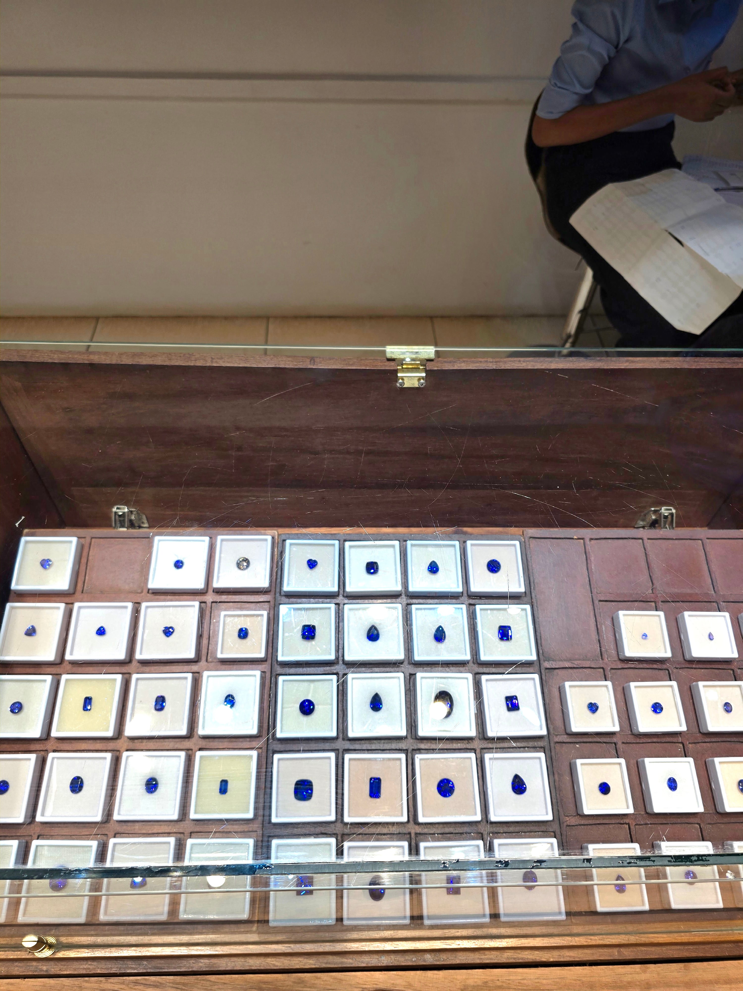 A display case showcasing various genuine Tanzanian gemstones and blue Tanzanite crystals.