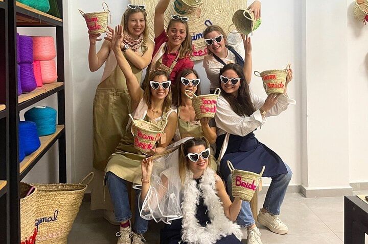 Group of young women in festive outfits posing with their personalized embroidered baskets and hats during a creative bachelorette workshop.
