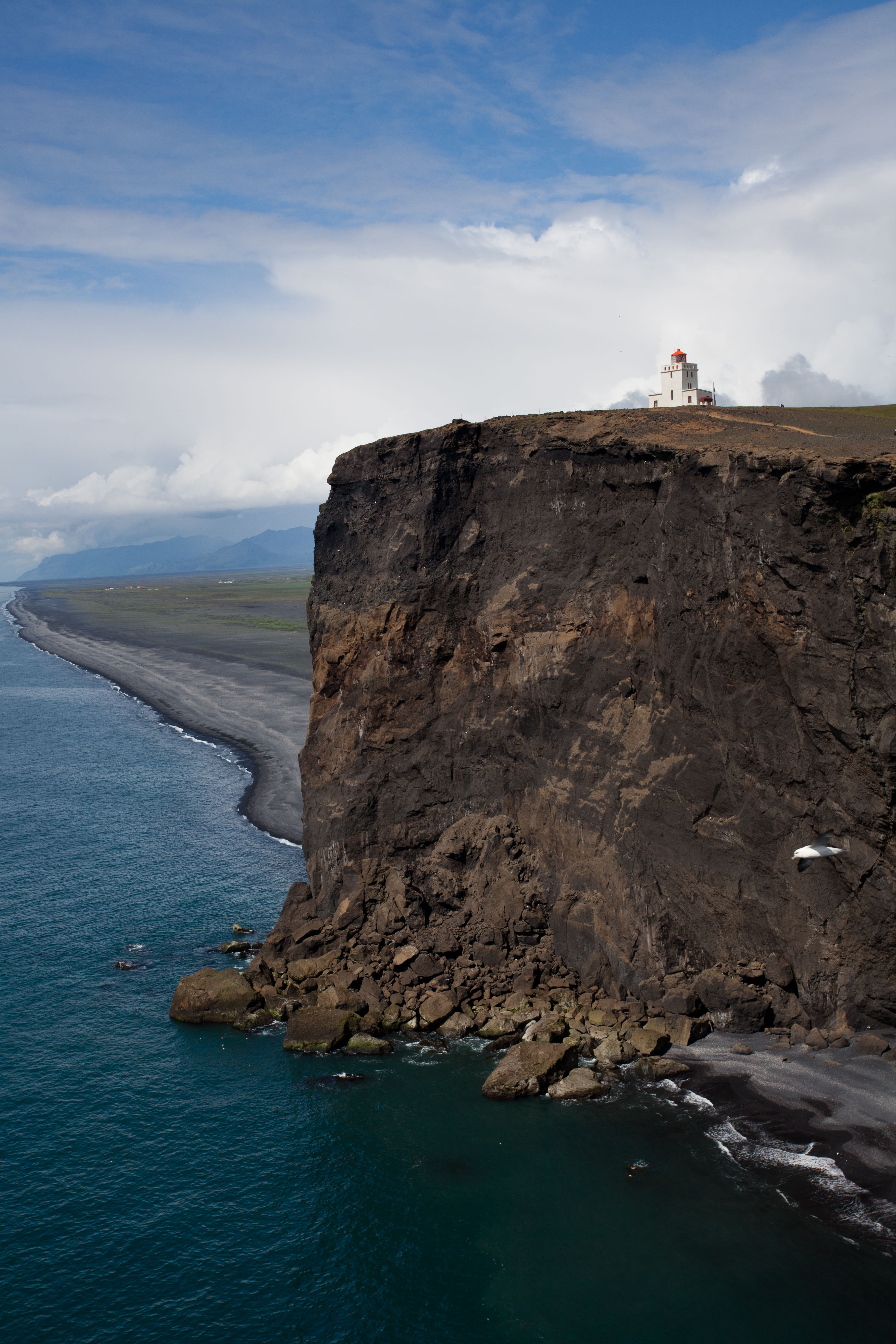 A Cliff with a lighthouse at the top next to Reynisfjara Black Sand Beach