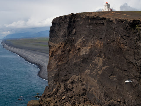 A Cliff with a lighthouse at the top next to Reynisfjara Black Sand Beach