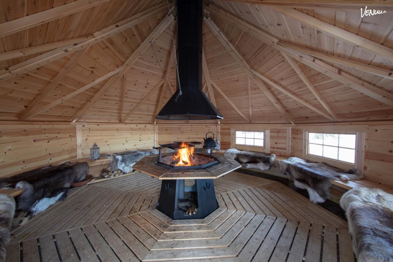 Interior of a traditional Lappish wooden kota with a central open fire, benches covered with reindeer hides