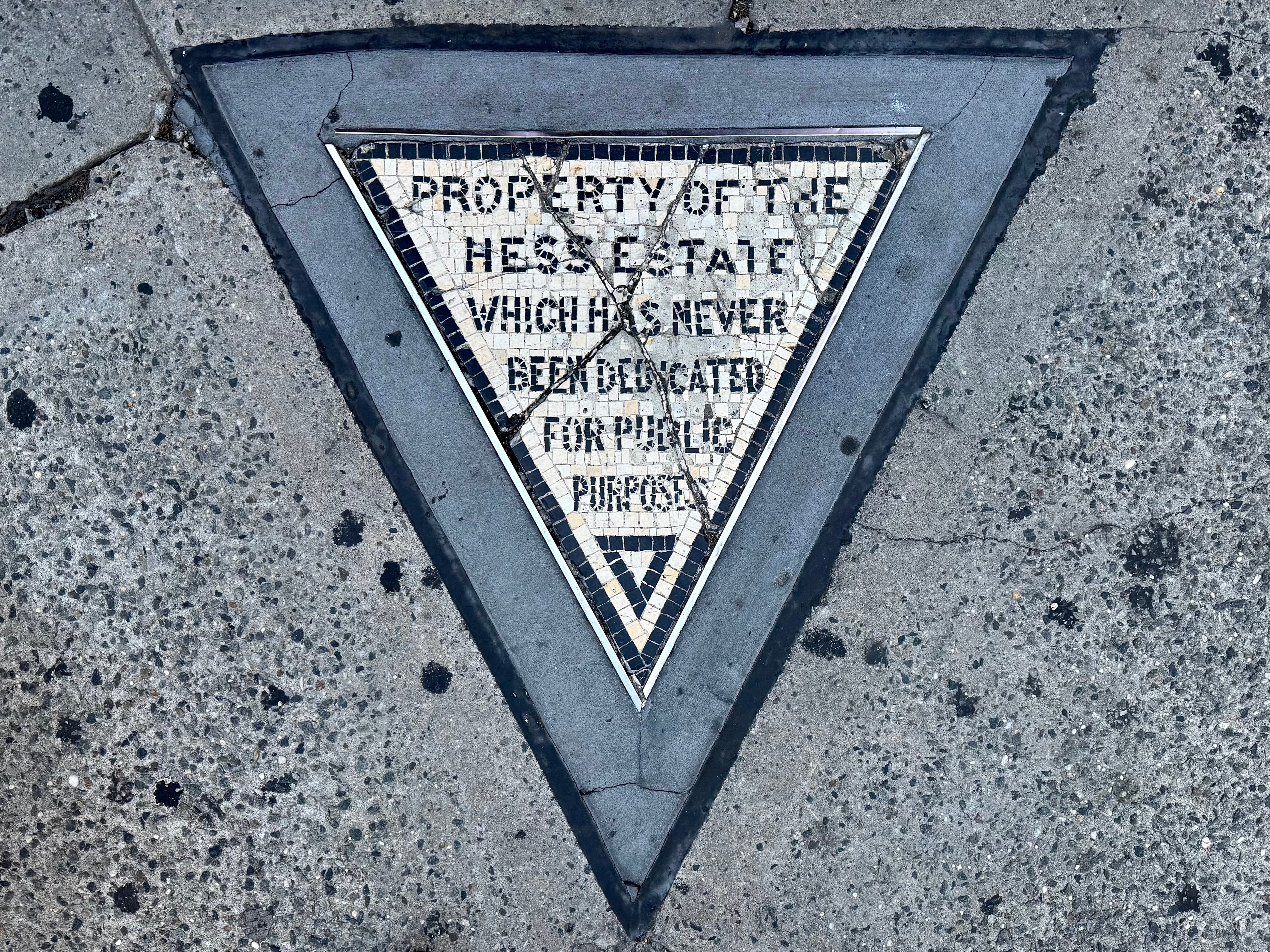 A triangular sidewalk plaque marking the former Hess Estate property.