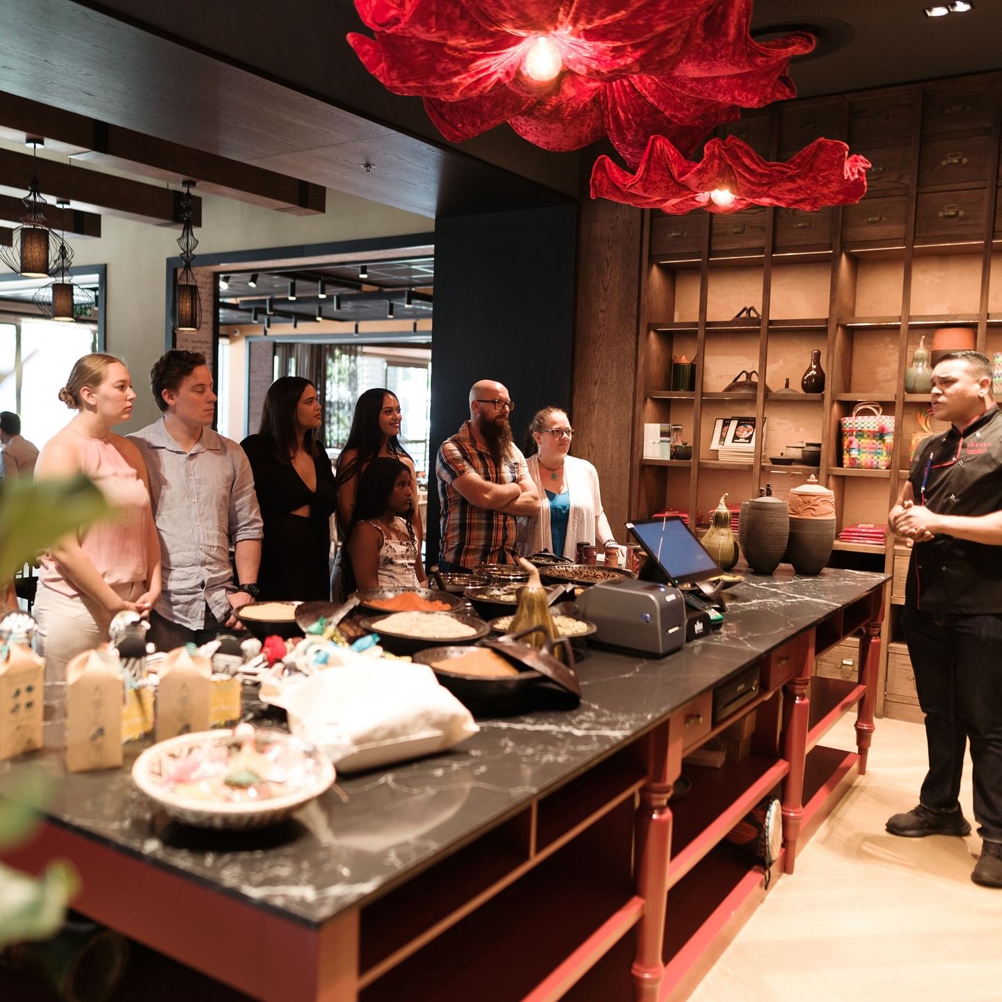 Indoor photo of a cooking class at SPYCED Restaurant. A chef is teaching a group behind a counter laden with bowls and ingredients.