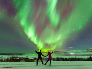 Two travellers striking a pose with northern lights in the background