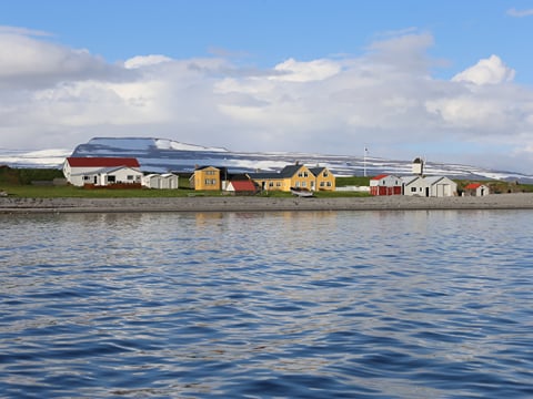 A cluster of brightly coloured buildings reflected in the water and the snow-covered mountainsides of the fjord visible beyond