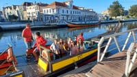 Travelers boarding colorful moliceiro boat on Aveiro canal beside waterfront buildings