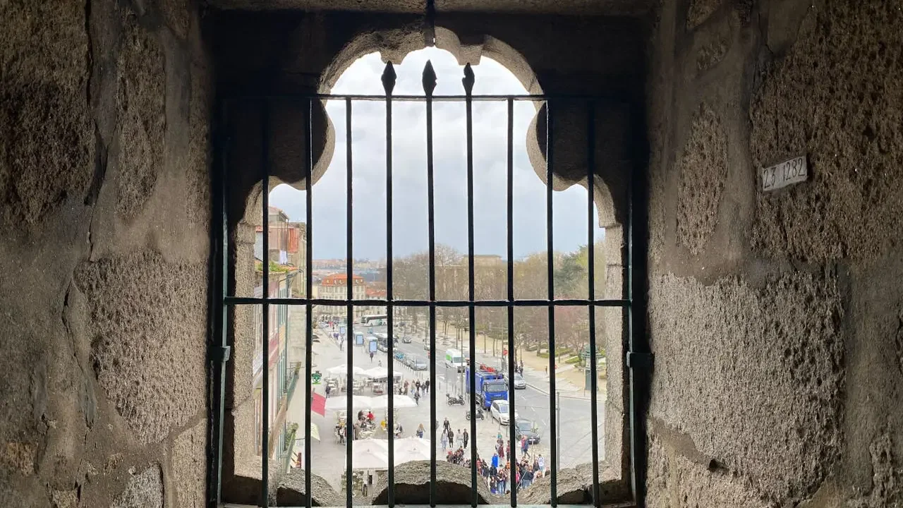 A view of a city square and street seen through a barred window framed by stone walls at Clérigos Tower & Museum Ticket.